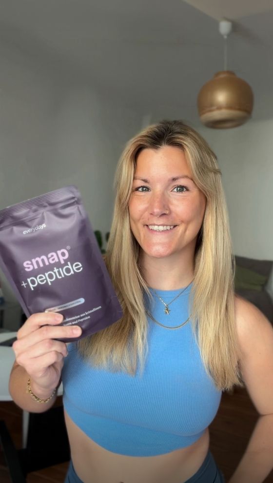 Creatorin mit blonden Haaren hält eine Packung smap +peptide in ihrer Wohnung