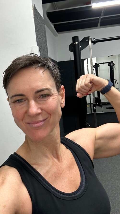 Creatorin lacht und spannt im Fitnessstudio den Bizeps an